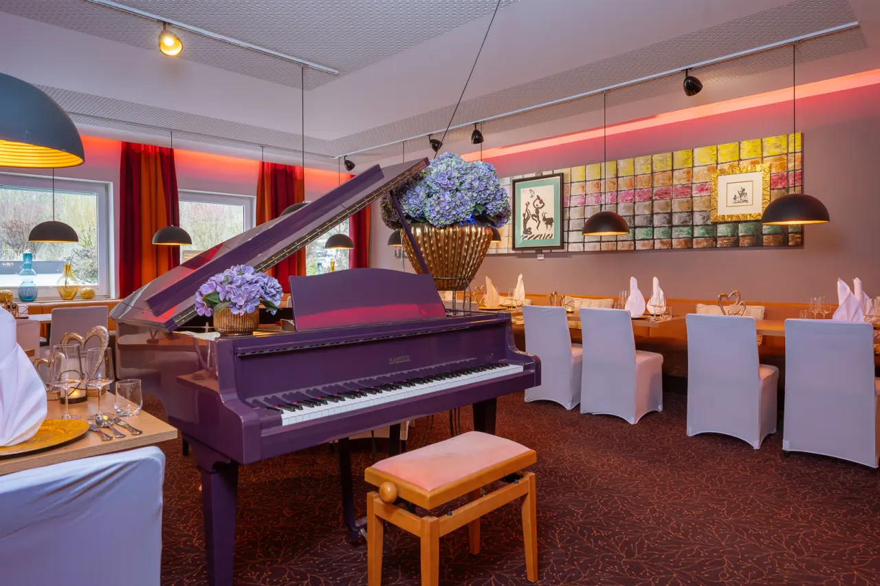 Elegantes Restaurant im Vitalhotel Sonneck mit lila Flügel, festlich gedeckten Tischen und moderner Kunst.