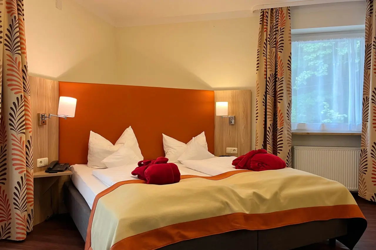Gemütliches Doppelzimmer mit orangefarbenem Kopfteil und Bademänteln im Vitalhotel Sonneck.