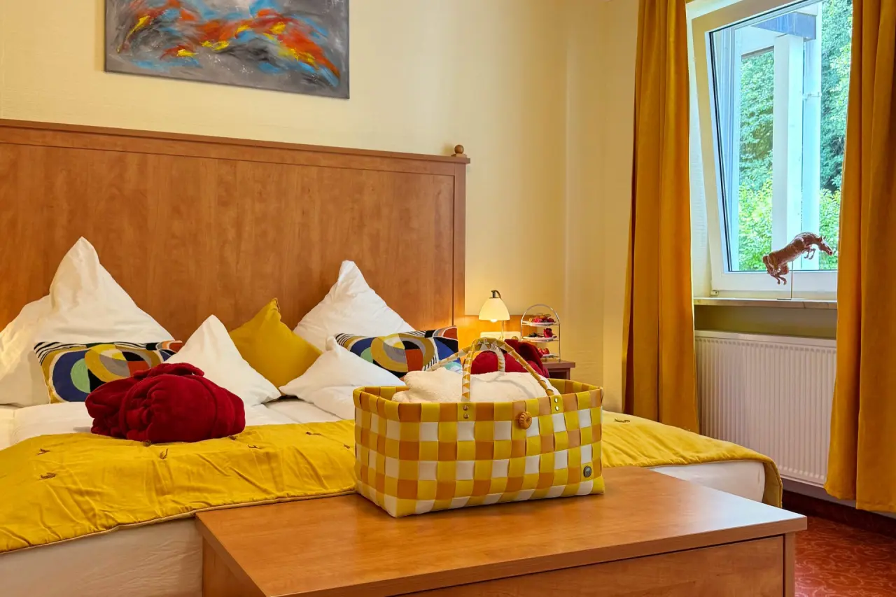 Gemütliches Hotelzimmer im Vitalhotel Sonneck mit Doppelbett, gelber Bettwäsche, Bademantel und Blick ins Grüne.