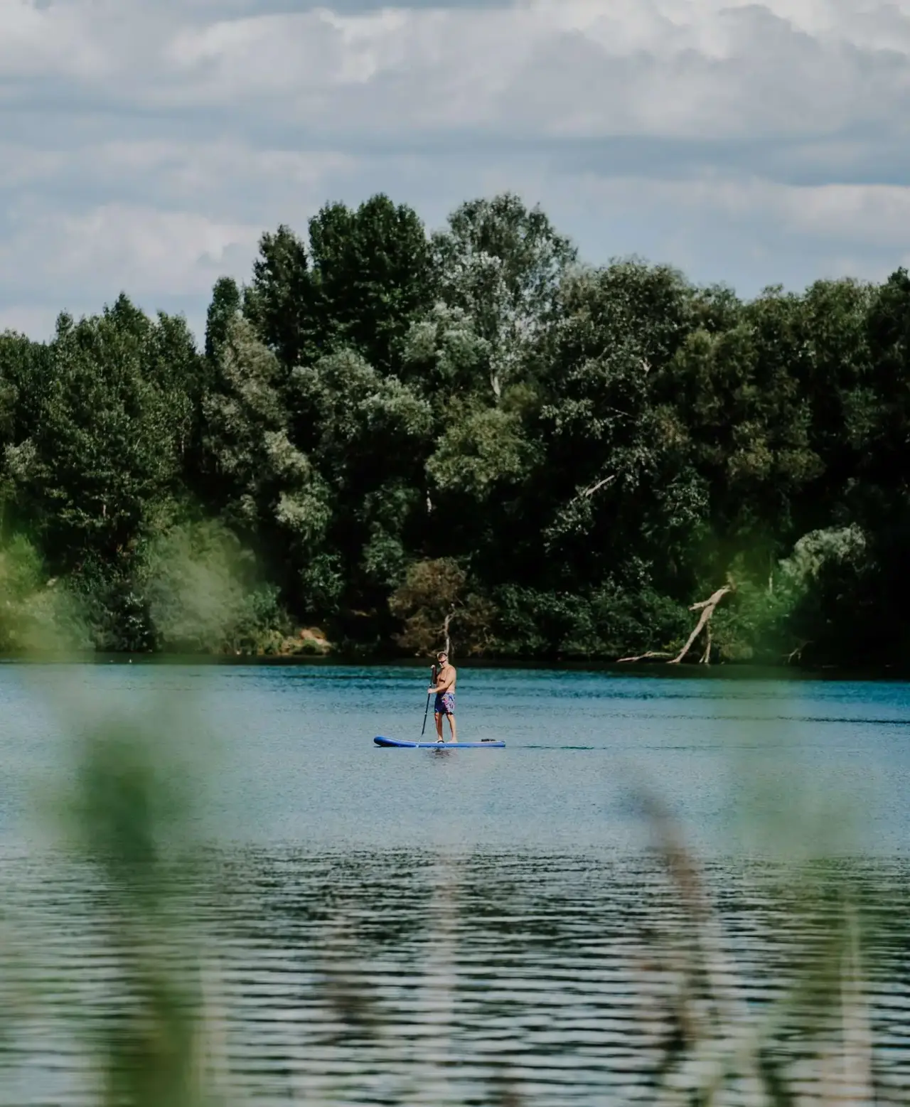 Person beim Stand-Up-Paddling auf dem Neuklostersee, umgeben von grünen Bäumen, am Seehotel am Neuklostersee.