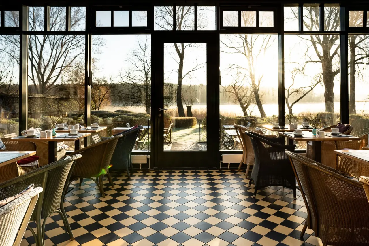 Sonnenverwöhnter Wintergarten im Seehotel am Neuklostersee mit Seeblick, kariertem Boden und einladenden Tischen.