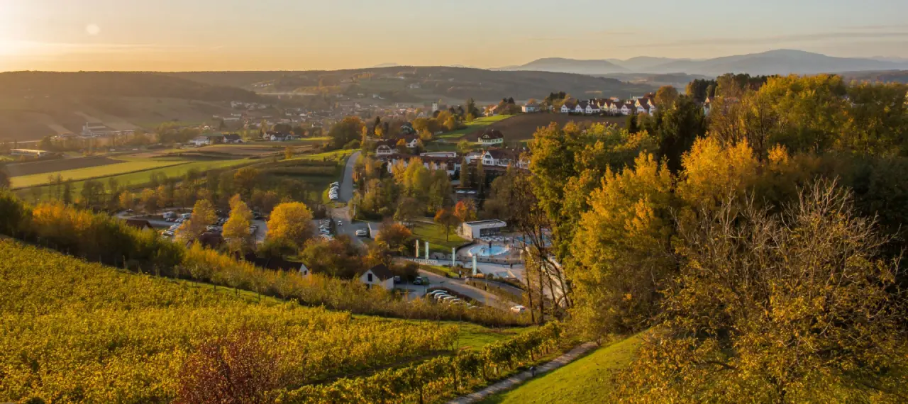 Herbstliches Panorama von Bad Waltersdorf mit Thermalbad und Weinbergen, umgeben von sanften Hügeln. Hotel & Spa Der Steirerhof.