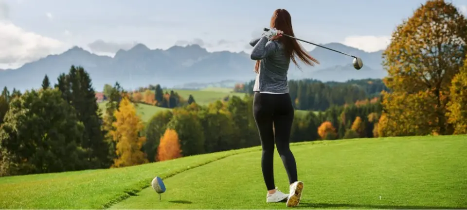 Frau beim Golfspiel auf dem Golfplatz des Hotel Auf der Gsteig mit Alpenpanorama im Herbst.