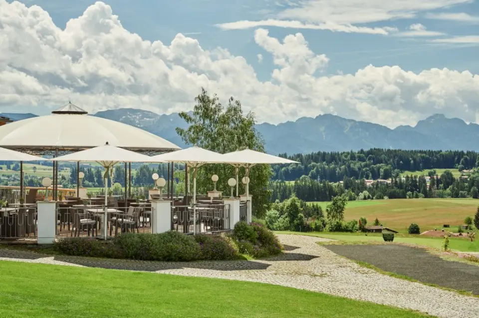 Sonnige Restaurantterrasse des Hotel Auf der Gsteig mit Tischen, Schirmen und weitem Blick auf die bayerischen Alpen.