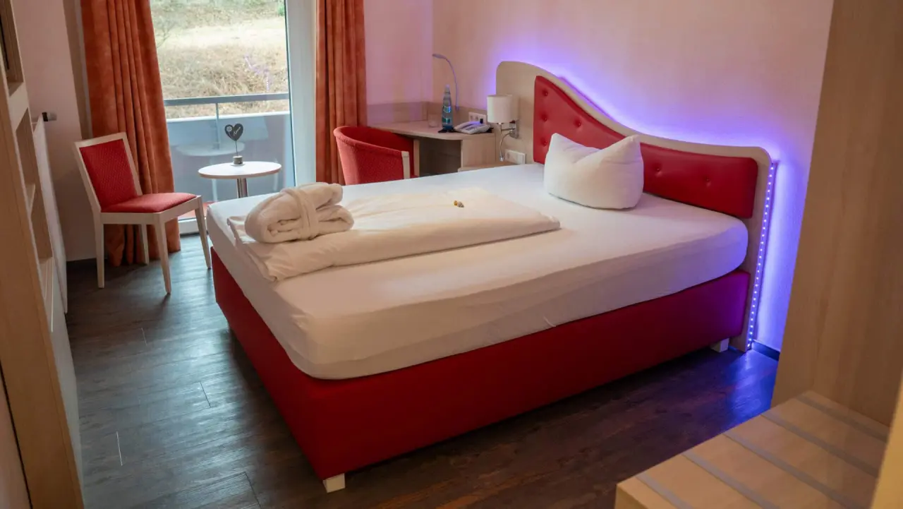 Gemütliches Doppelzimmer im Kurhotel Hochsauerland 2010 mit rotem Bett, Balkon und indirekter Beleuchtung.