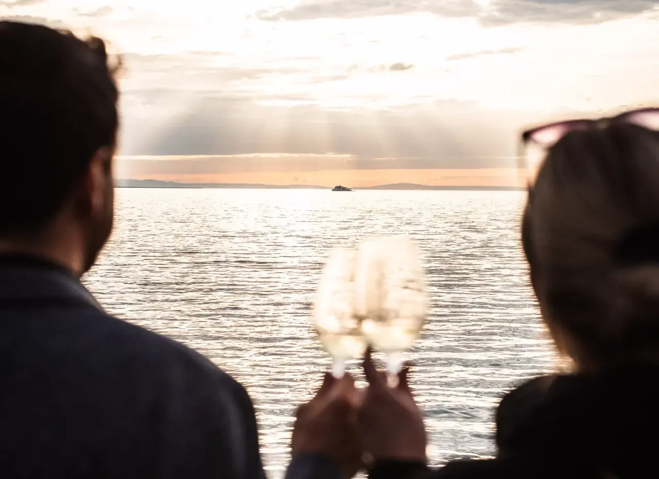 Romantischer Sonnenuntergang am See mit einem Paar, das mit Sekt anstösst, im Seehotel Am Kaiserstrand.