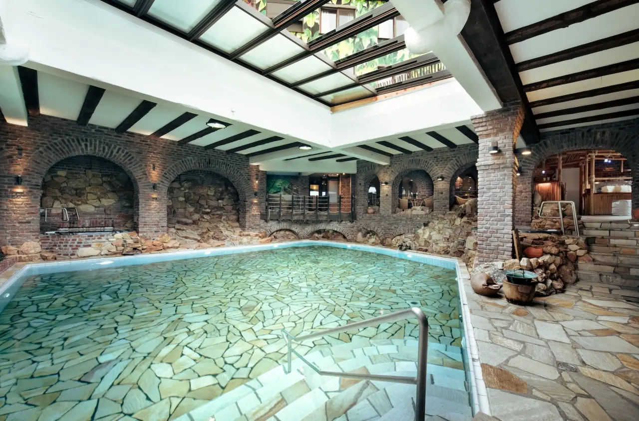 Rustikaler Innenpool mit Steinwänden und Glasdach im Wellnessbereich des Land Gut Höhne Hotels.