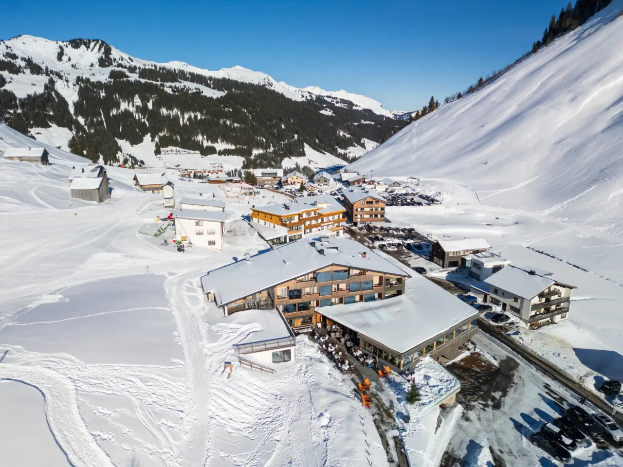 Alpenresort Walsertal im Winter: Luftaufnahme des Hotels in verschneiter Berglandschaft mit sonnigem Himmel.