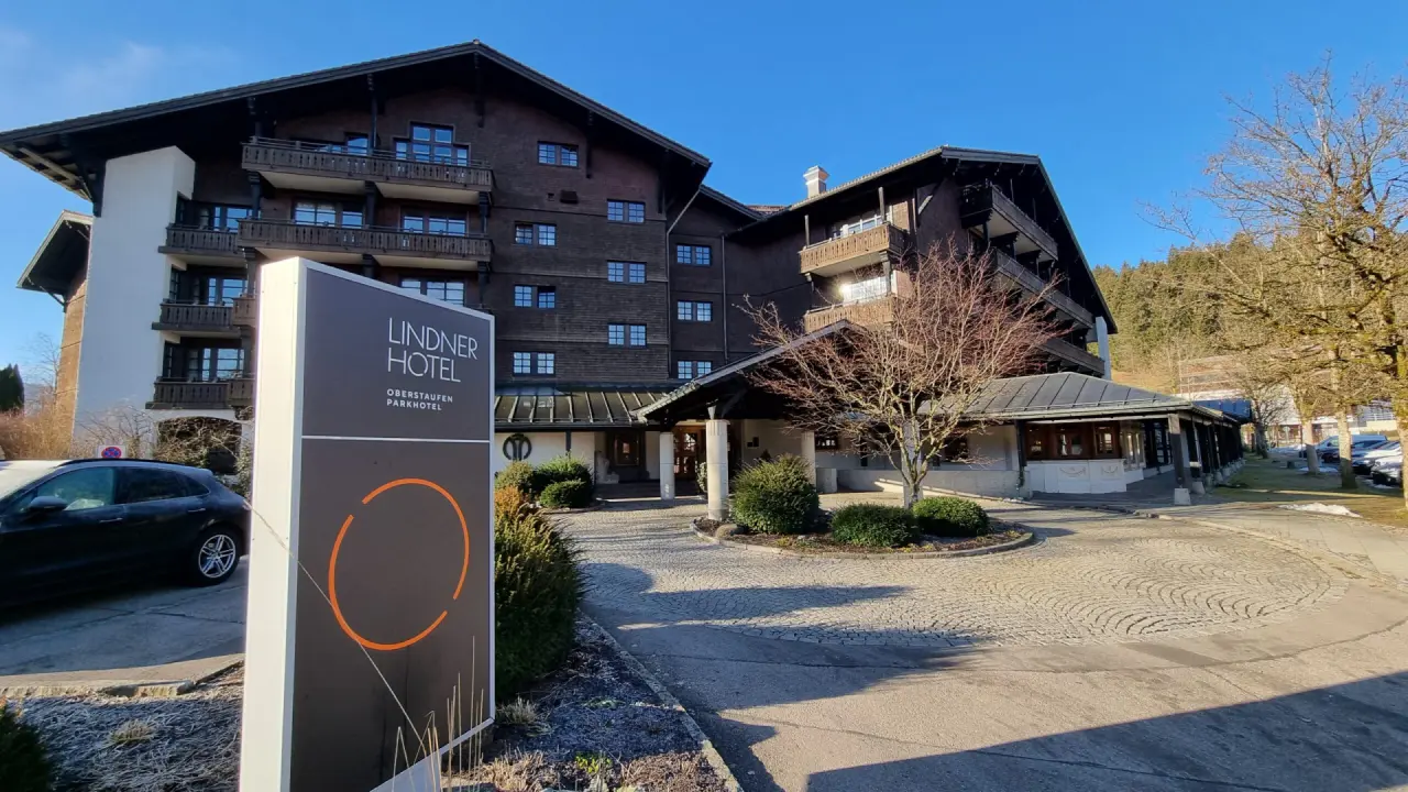 Aussenansicht des Lindner Hotel Oberstaufen Parkhotel mit Hotel-Schild und Zufahrt an einem sonnigen Wintertag.