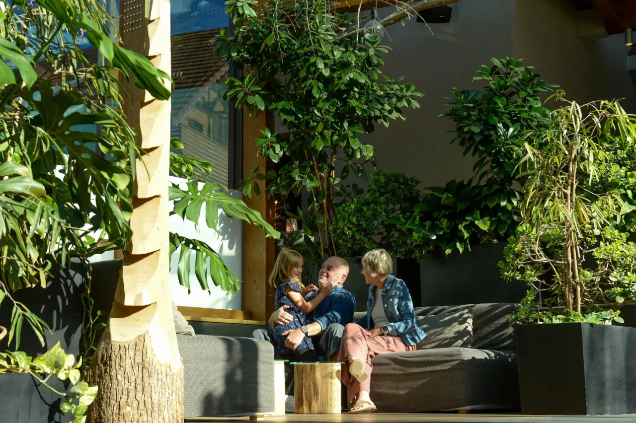 Familie (Grosseltern mit Enkelin) entspannt auf einer Couch in der grünen Lounge des Ulrichshof Baby & Kinder Bio-Resort.