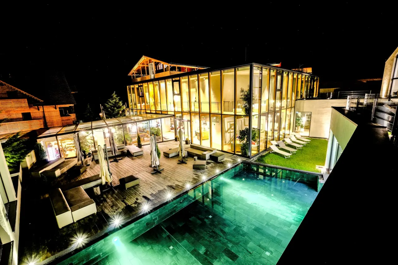 Nachtansicht des modernen Ulrichshof Baby & Kinder Bio-Resort mit beleuchtetem Aussenpool und Lounge-Bereich.