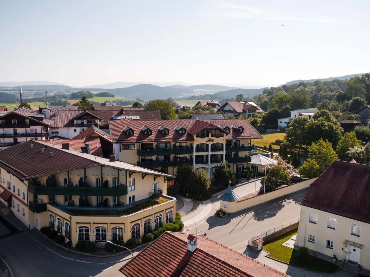 Luftaufnahme des Posthotel mit roten Dächern und grünen Balkonen, umgeben von einer ländlichen Hügellandschaft.