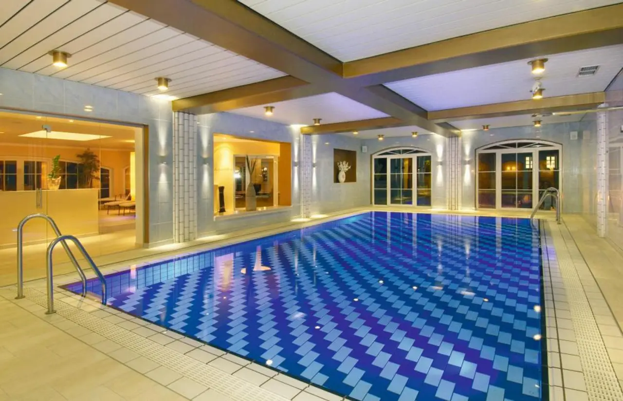 Grosszügiger Innenpool mit blauen Mosaikfliesen und warmem Licht im Posthotel. Ideal für Entspannung und Schwimmen.