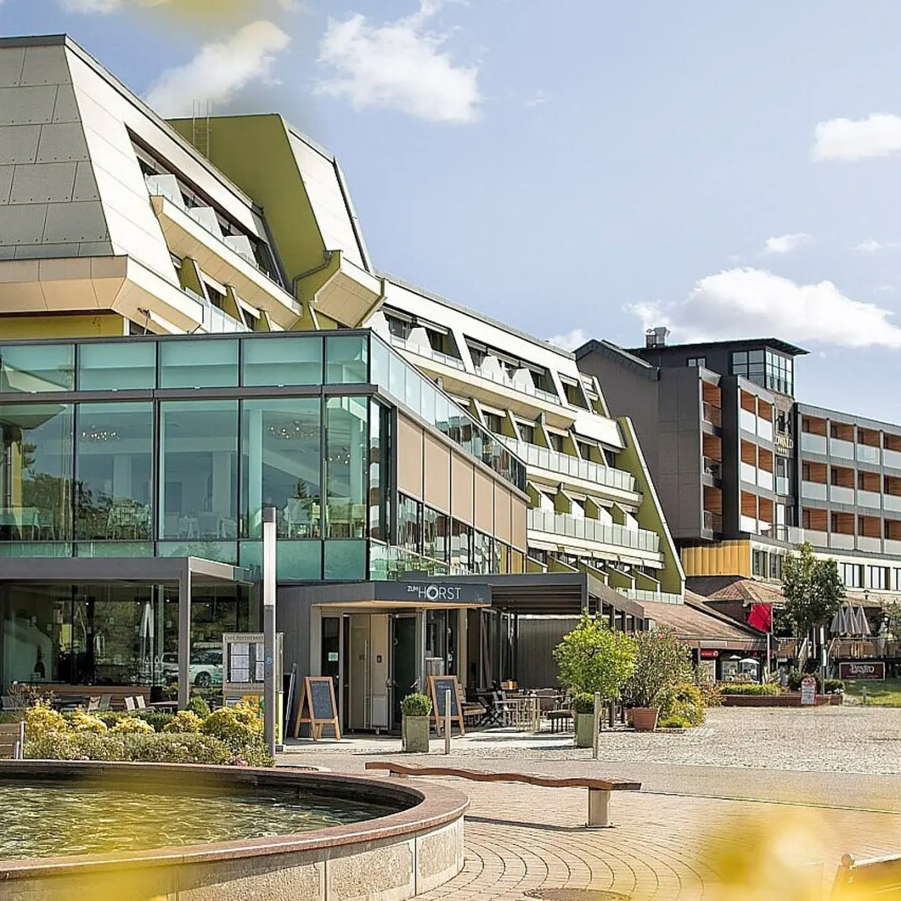 Aussenansicht des modernen Thermenhotel Vier Jahreszeiten Loipersdorf mit Restaurant und Brunnen an einem sonnigen Tag.