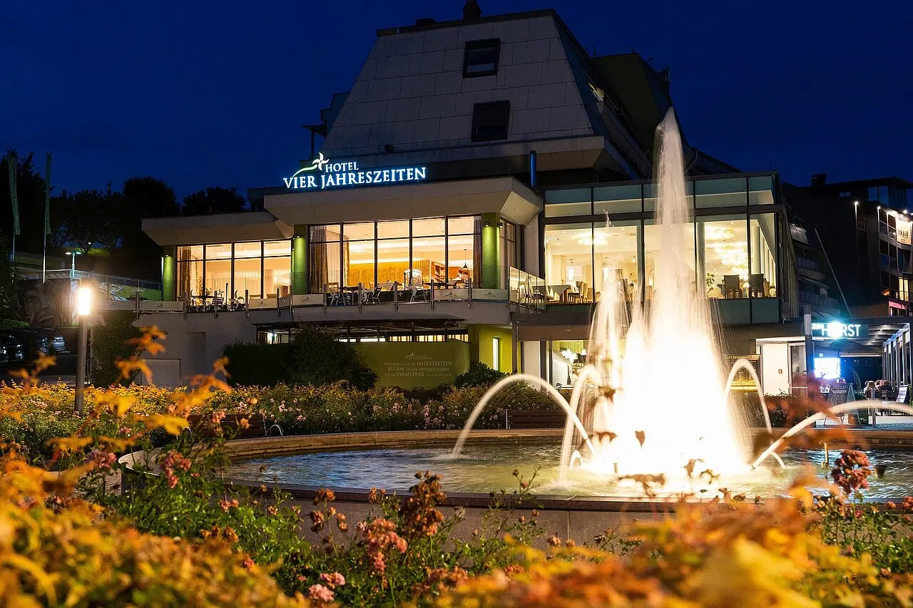 Nachtaufnahme des Thermenhotel Vier Jahreszeiten Loipersdorf mit beleuchtetem Hotelgebäude und Springbrunnen im Vordergrund.