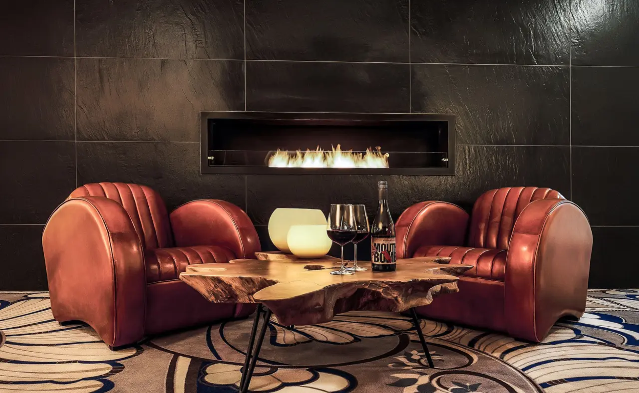 Gemütliche Lounge im Hotel Das Aunhamer mit modernem Kamin, Ledersesseln und rustikalem Holztisch für entspannte Abende.