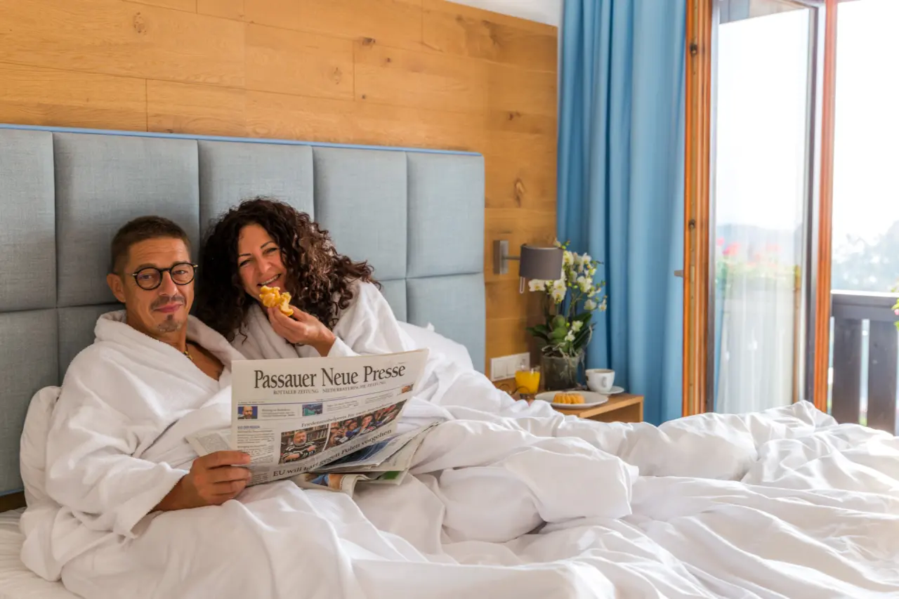 Glückliches Paar im Bademantel beim Frühstück im gemütlichen Hotelzimmer mit Balkon im Das Aunhamer.