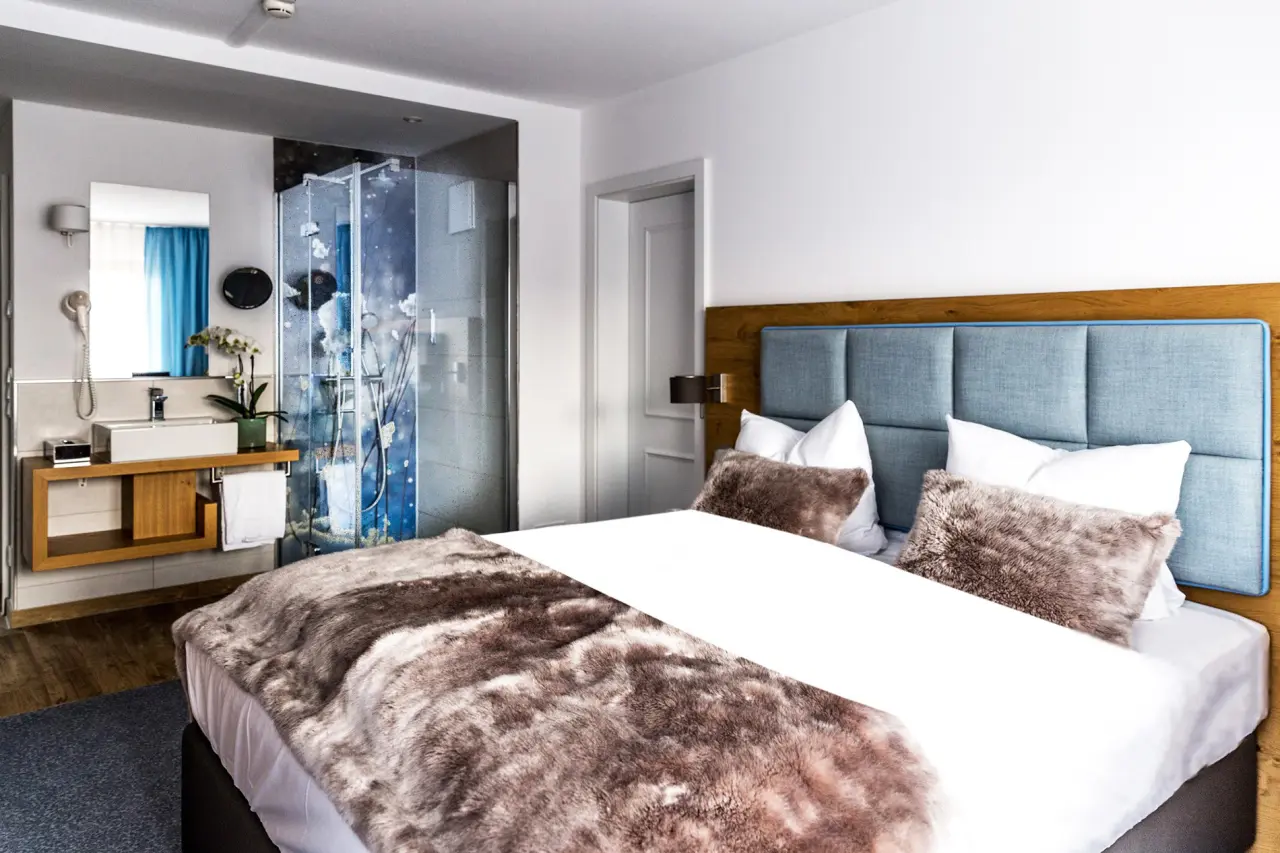 Modernes Hotelzimmer im Das Aunhamer mit komfortablem Bett, offenem Badbereich und stilvoller Einrichtung.