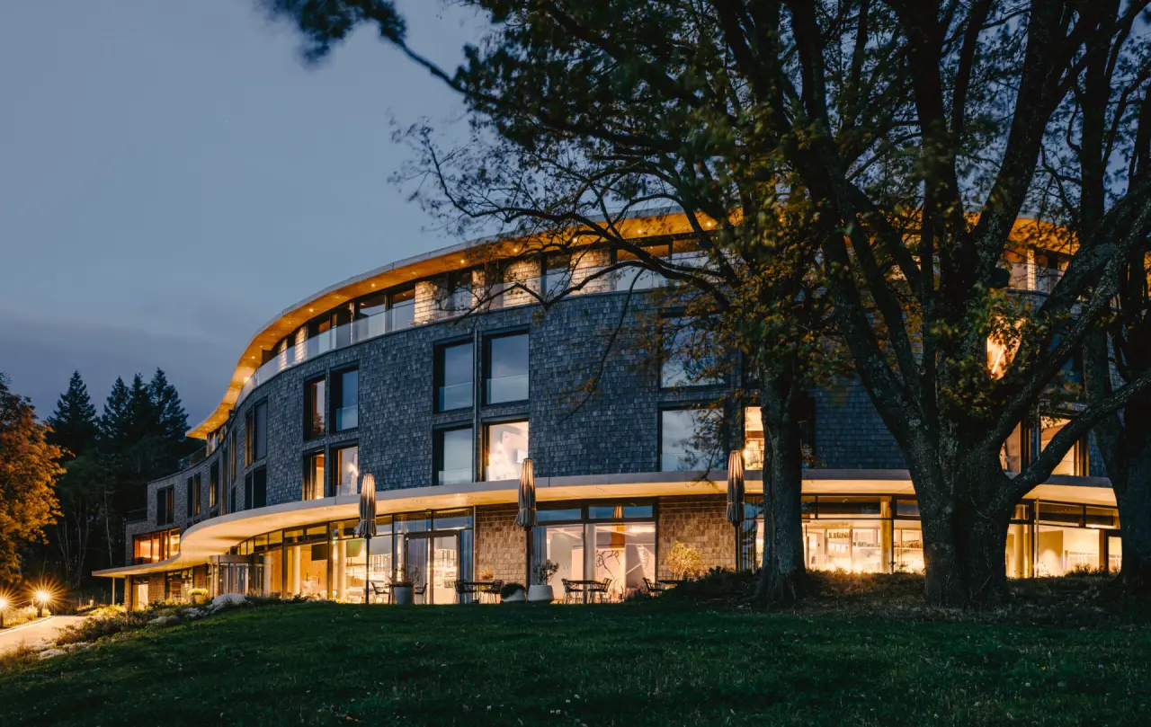 Modernes Gesundheitsresort Luisenhöhe im Schwarzwald bei Abenddämmerung. Die beleuchtete Fassade fügt sich in die Natur ein.
