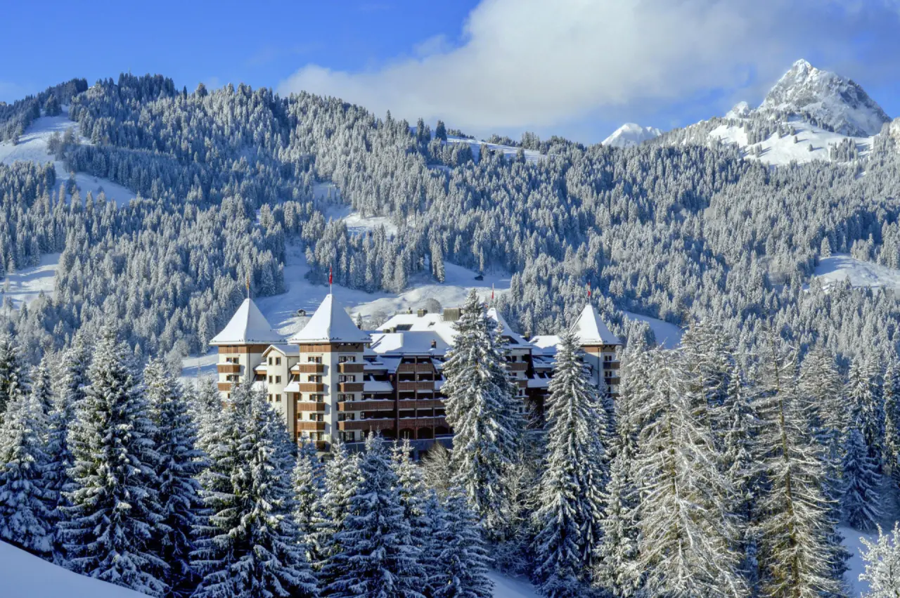 The Alpina Gstaad: Luxuriöses Hotel in verschneiter Alpenlandschaft mit Tannenwäldern und Berggipfeln.