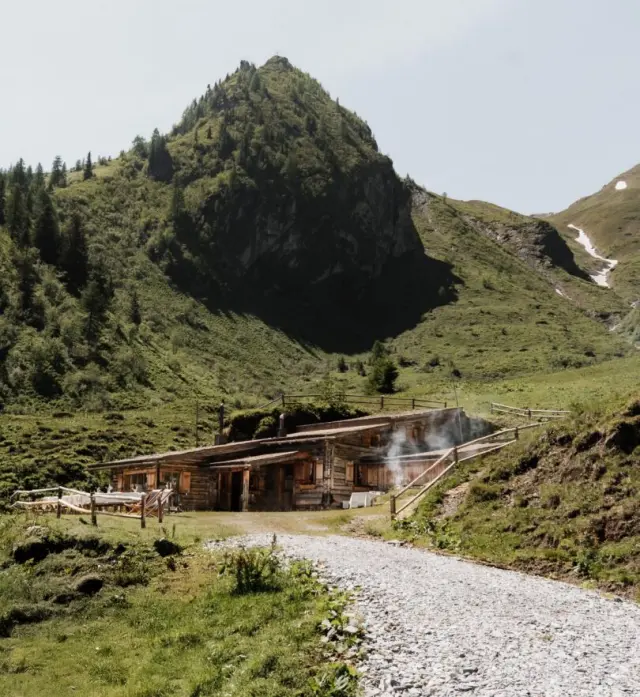Rustikale Berghütte mit rauchendem Kamin und alpiner Landschaft im Familien Natur Resort Moar Gut.