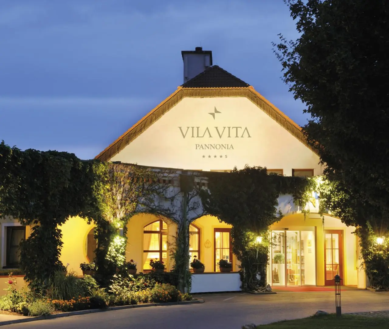 Beleuchtete Aussenansicht des VILA VITA Pannonia Hotels bei Dämmerung mit einladendem Eingangsbereich.