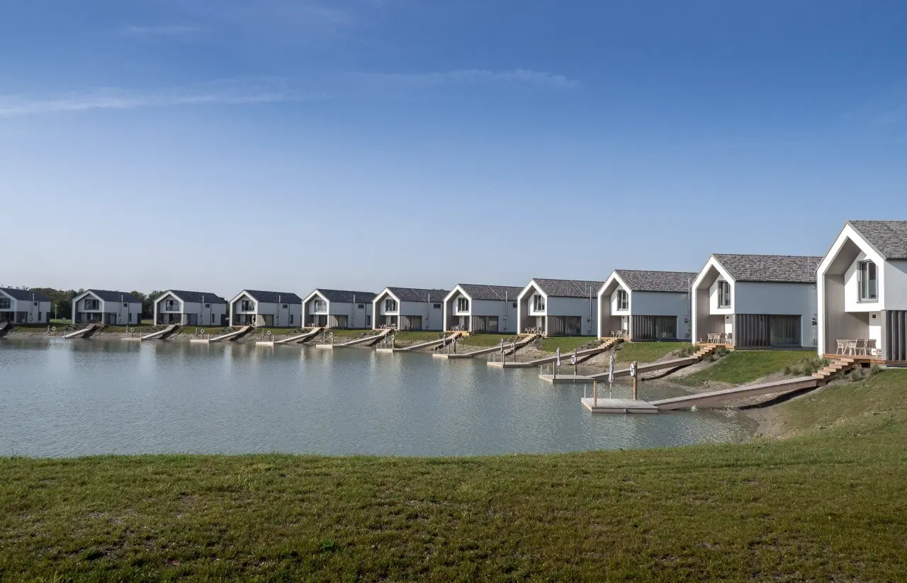 Moderne Seehäuser mit privaten Stegen am Wasser der VILA VITA Pannonia Anlage unter blauem Himmel.