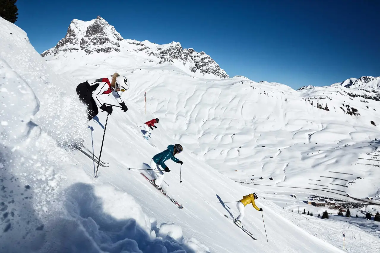 Dynamische Skifahrer auf einer verschneiten Piste mit majestätischem Bergpanorama, ideal für Winterurlaub im Hotel Am Holand.