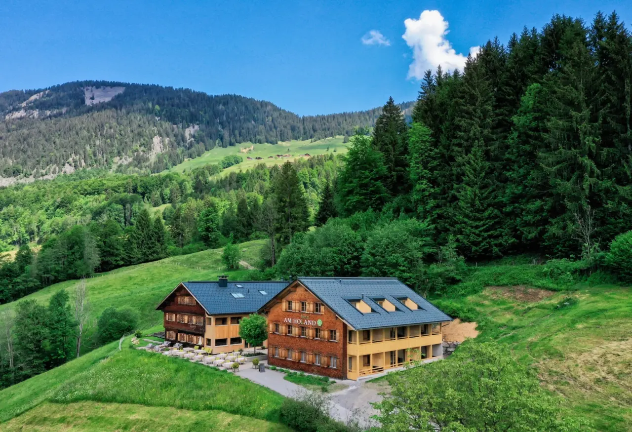Hotel Am Holand in den grünen Bergen, umgeben von Wäldern und Wiesen unter blauem Himmel.