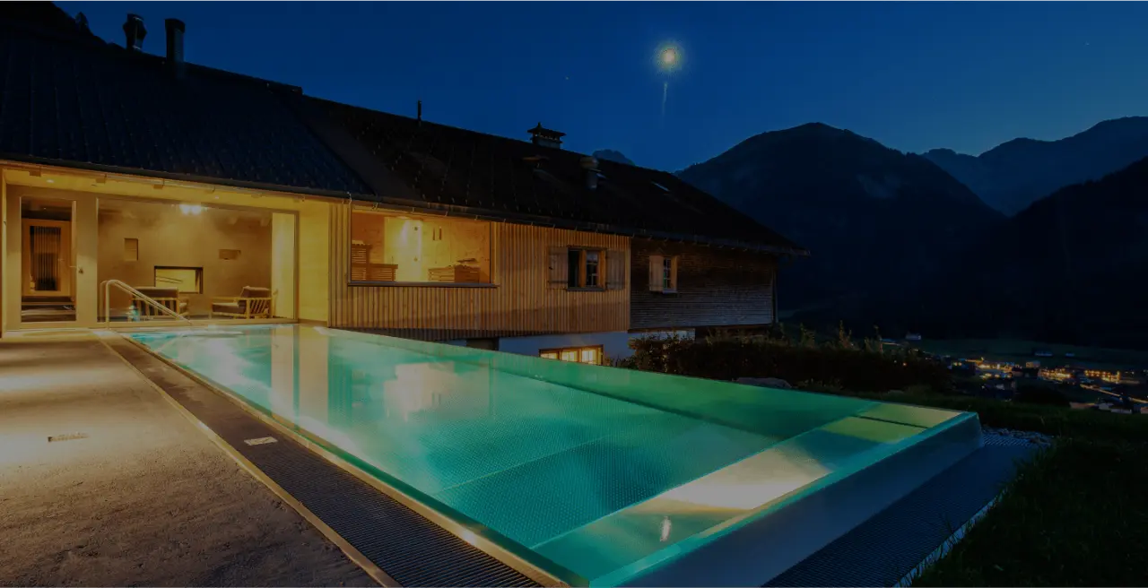 Beleuchteter Infinity-Pool des Hotel Am Holand bei Nacht mit Blick auf die umliegenden Berge und das Tal.