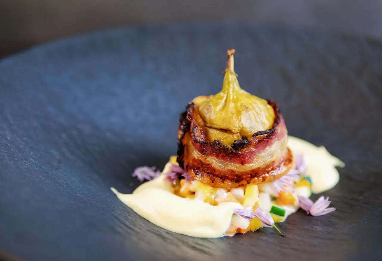 Ansprechend angerichteter Hauptgang mit Feige und Speck auf dunklem Teller im Restaurant des Hotel Am Holand.