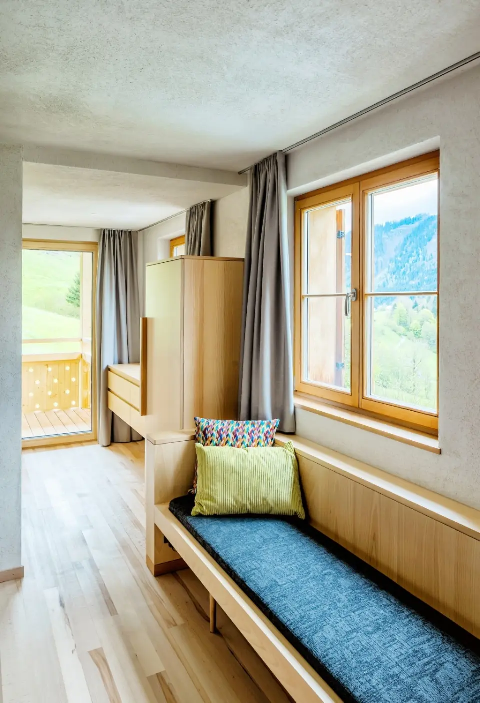 Gemütliches Hotelzimmer im Hotel Am Holand mit Holzeinrichtung, Sitzbank und Balkonblick auf die Berge.