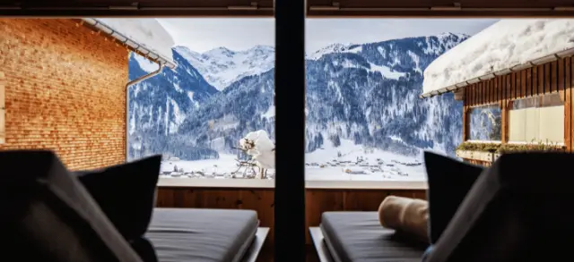 Entspannungsbereich mit Liegen und Panoramablick auf die verschneiten Alpen im Hotel Am Holand.