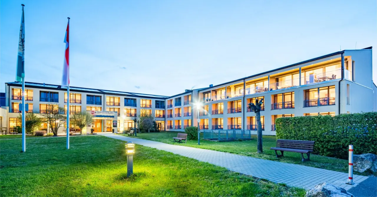 Aussenansicht des Best Western Plus Kurhotel an der Obermaintherme bei Dämmerung mit beleuchteten Balkonen und Gartenweg.
