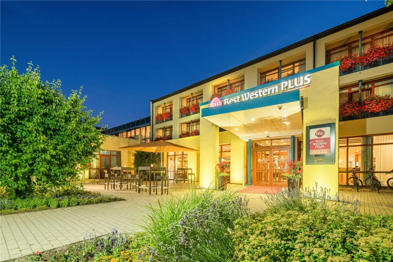 Aussenansicht des Best Western Plus Kurhotel an der Obermaintherme bei Abenddämmerung mit beleuchtetem Eingang und Terrasse.