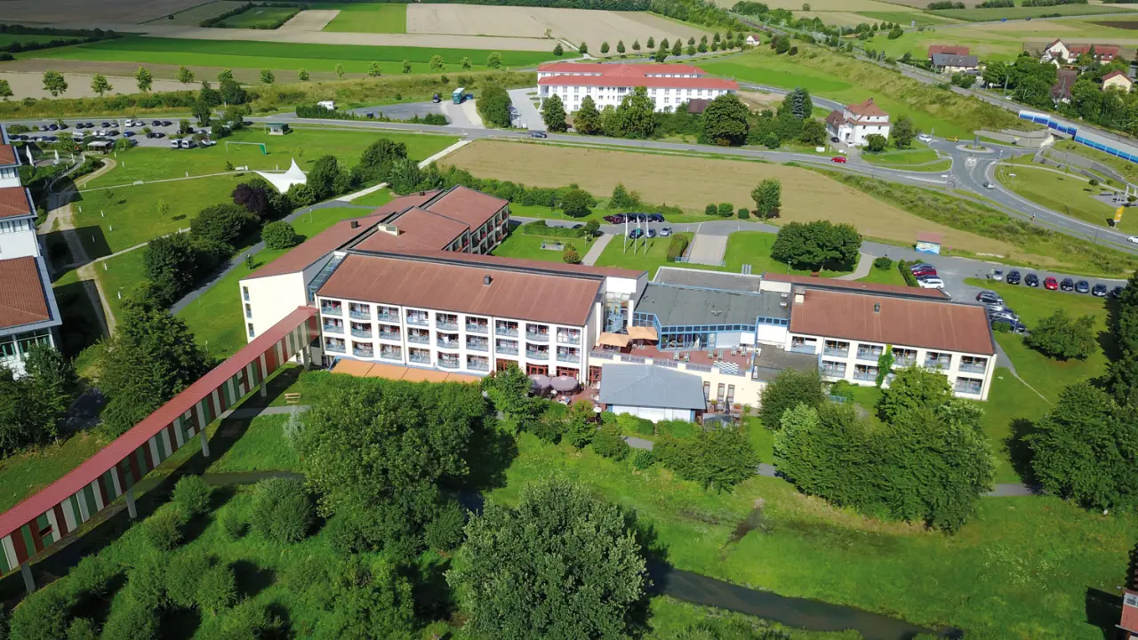 Luftaufnahme des Best Western Plus Kurhotel an der Obermaintherme mit Hotelkomplex, grüner Landschaft und Verbindungsbrücke.
