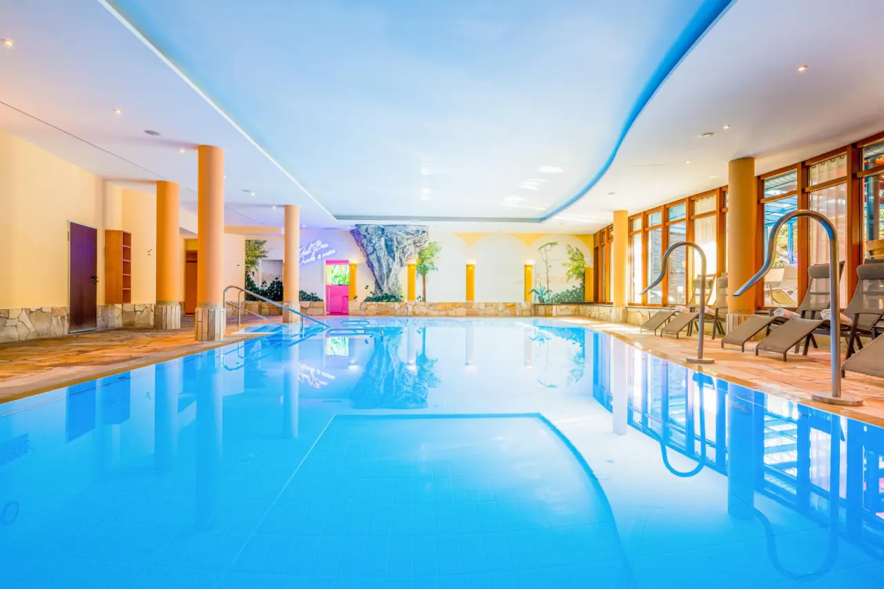 Grosszügiger Innenpool mit Liegebereich und tropischer Wandgestaltung im Best Western Plus Kurhotel an der Obermaintherme.