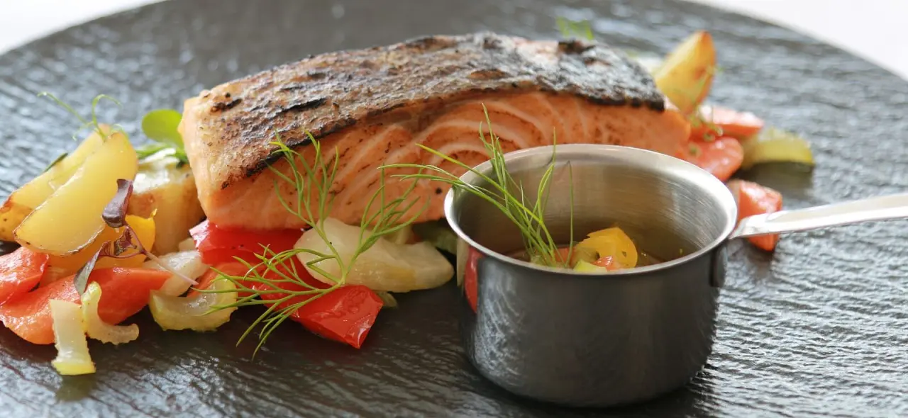 Gebratenes Lachsfilet mit Gemüse und Sauce auf einem Schiefer-Teller im Restaurant des Parkhotel Weiskirchen.