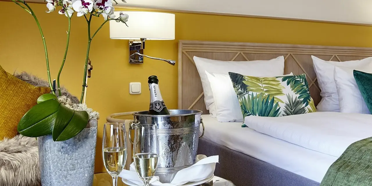 Gemütliches Hotelzimmer im Parkhotel Weiskirchen mit Doppelbett, floralen Akzenten und gekühltem Sekt als Willkommensgruß.