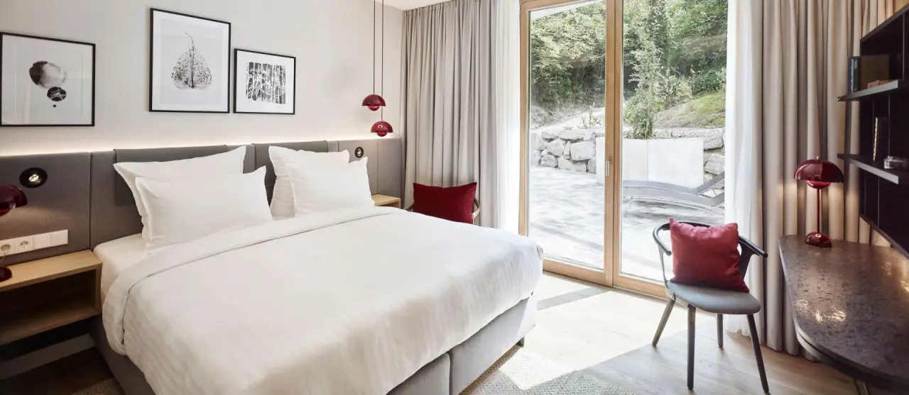 Modernes Hotelzimmer mit Doppelbett, roter Dekoration und Zugang zur Terrasse im Steigenberger Hotel and Spa Krems.