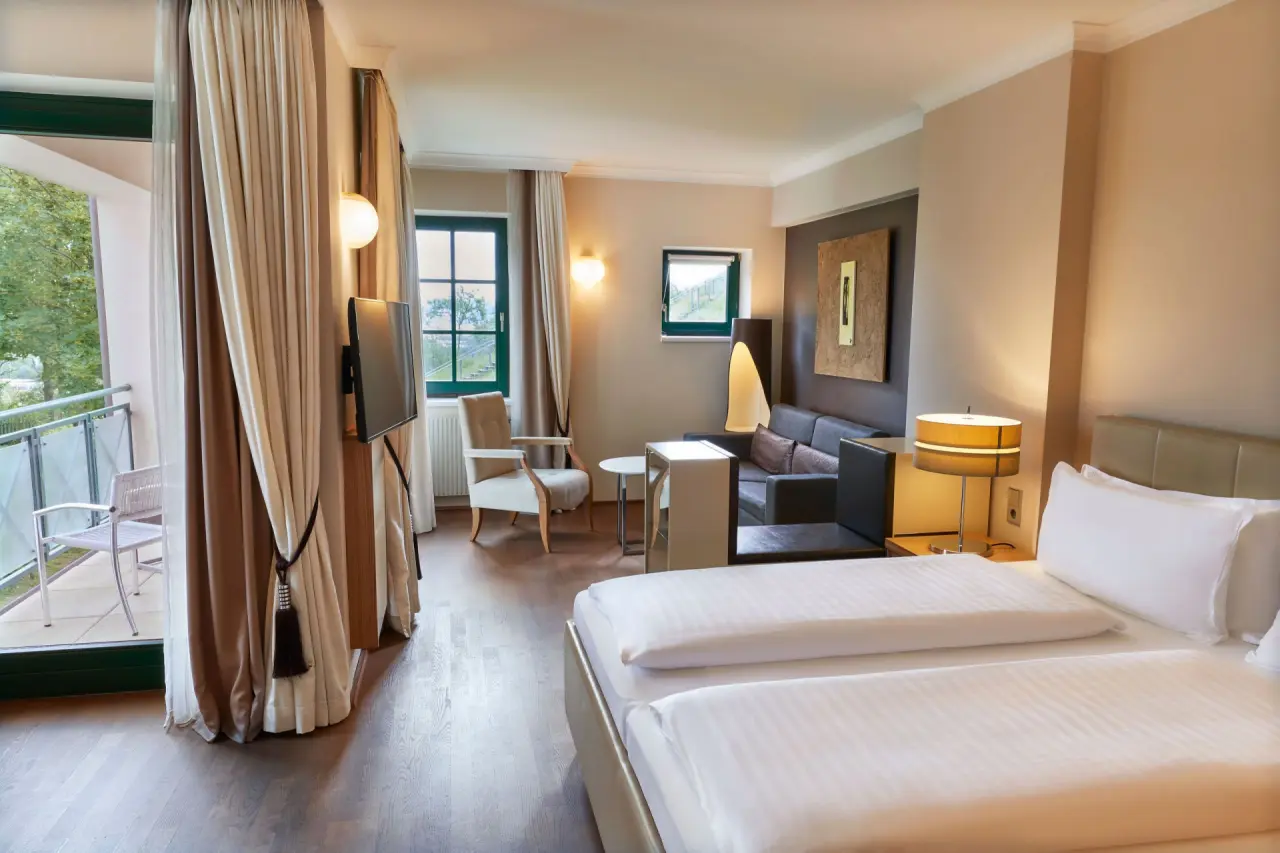 Geräumiges Hotelzimmer mit Doppelbett, Sitzbereich und Balkon im Steigenberger Hotel and Spa Krems.