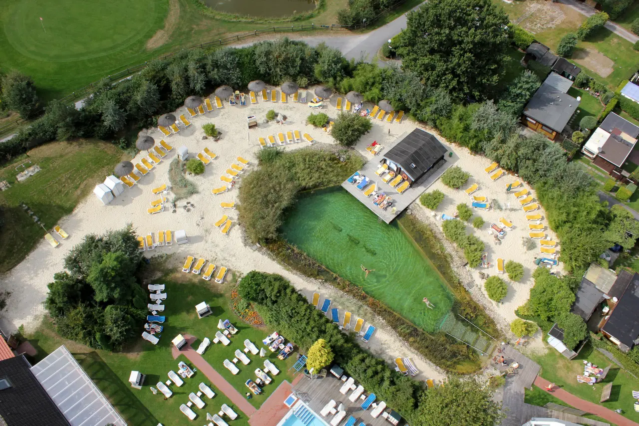 Luftaufnahme des Naturbadeteichs mit Sandstrand, Liegebereich und Pool im Jammertal-Resort.