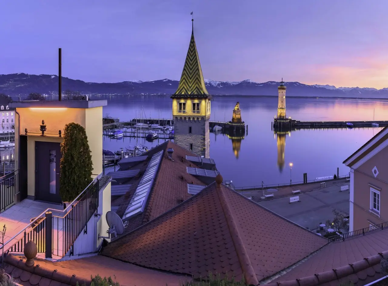 Abendliche Panoramaaussicht auf den Lindauer Hafen mit Leuchtturm und Mangturm vom Hotel Helvetia am Bodensee.