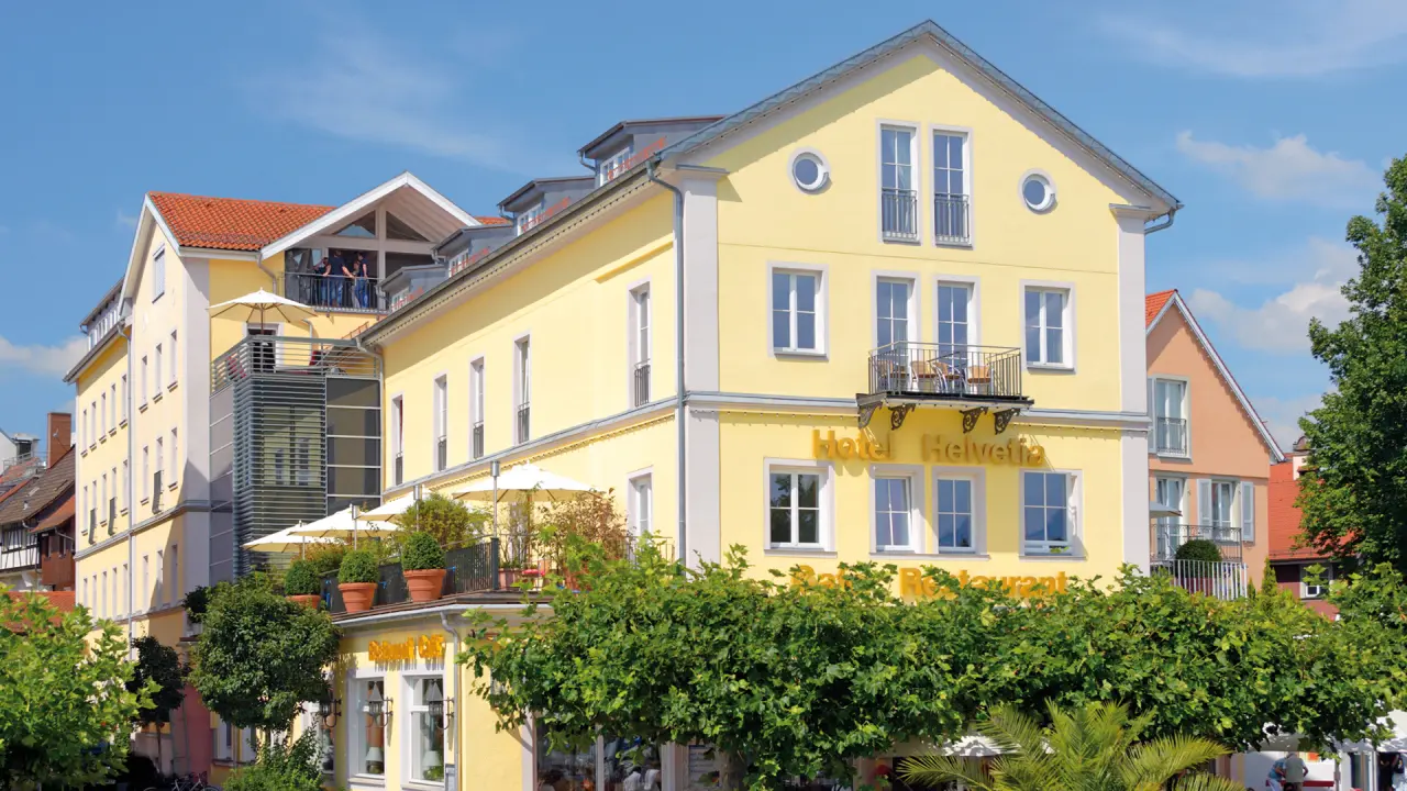 Aussenansicht des gelben Hotel Helvetia Gebäudes mit Balkonen und Terrassen unter blauem Himmel.