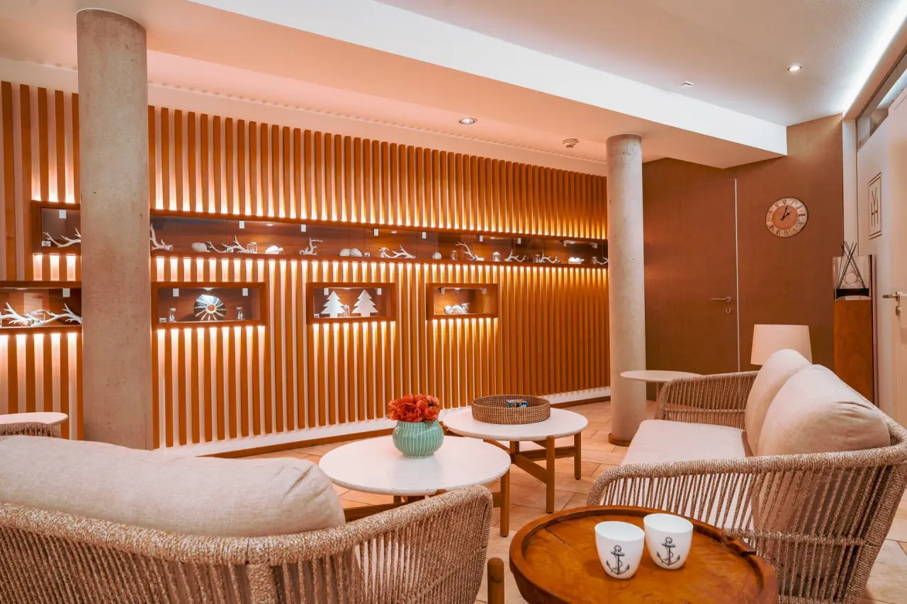 Stilvolle Hotellounge im Hotel Helvetia mit Holzlamellenwand, beleuchteten Nischen und bequemen Rattan-Sesseln für entspannte Momente.