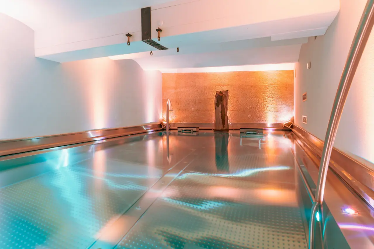 Modernes Hallenbad mit stimmungsvoller Beleuchtung und Natursteinwand im Wellnessbereich des Hotel Helvetia.