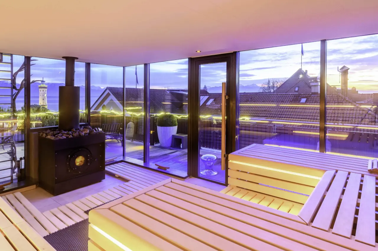 Moderne Sauna im Hotel Helvetia mit Panoramablick auf den Bodensee, den Lindauer Leuchtturm und die Alpen bei Sonnenuntergang.