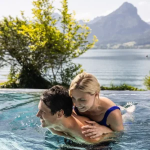 Glückliches Paar im Infinity Pool des Hotel Seevilla Wolfgangsee mit Blick auf den See und die Berge.
