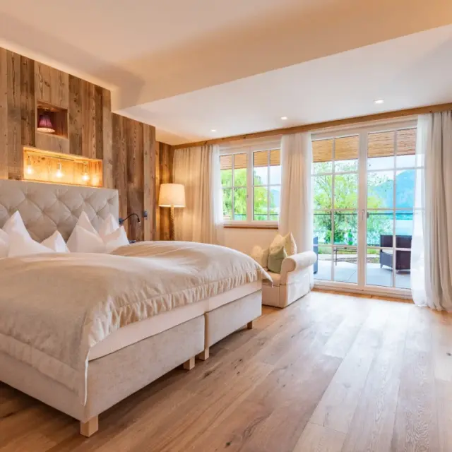 Modernes Hotelzimmer im Hotel Seevilla Wolfgangsee mit Holzwand, gemütlichem Bett und Balkon mit Panoramablick auf den Wolfgangsee.