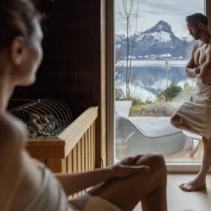 Paar entspannt in der Sauna mit Panoramablick auf den Wolfgangsee und die verschneiten Berge im Hotel Seevilla Wolfgangsee.